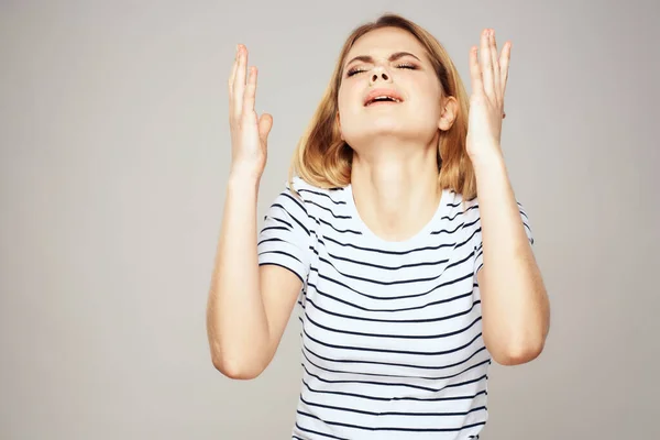 Eine Frau im gestreiften T-Shirt hält ihre Hände vor ihrem emotionalen Unbehagen hellen Hintergrund — Stockfoto