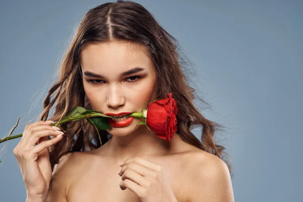 Portrait d'une femme avec une rose rouge dans les mains sur un fond gris épaules nues maquillage du soir — Photo