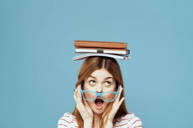 Kafası üzerine kitapları olan kız öğrenci. Bilim eğitimi almış. Mavi arka plan duyguları elleriyle hareket ediyor.