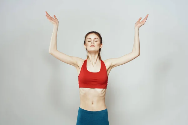 Een vrouw in een rood T-shirt op een lichte achtergrond is bezig met fitness gebaren met haar handen een slank figuur — Stockfoto