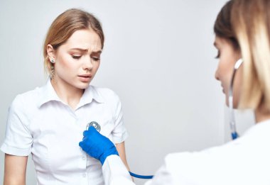 Bir hasta sandalyeye oturur ve steteskoplu bir kadın doktor