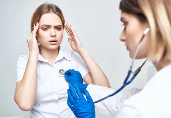 Woman patient complains of headache to doctor with stethoscope
