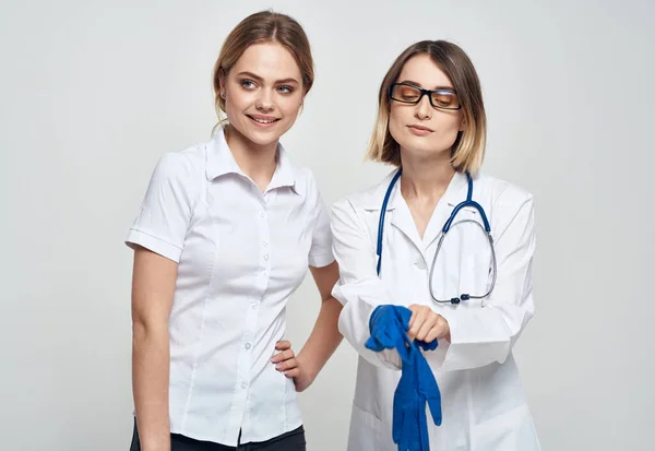 Kobieta-lekarz w sukni medycznej i niebieskich rękawiczkach ze stetoskopem na szyi i pacjentką — Zdjęcie stockowe