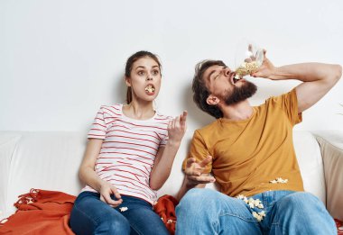 Patlamış mısır yiyen bir adam ve güzel bir kadın parlak bir odada aile dostlarıyla iletişim kuruyor.