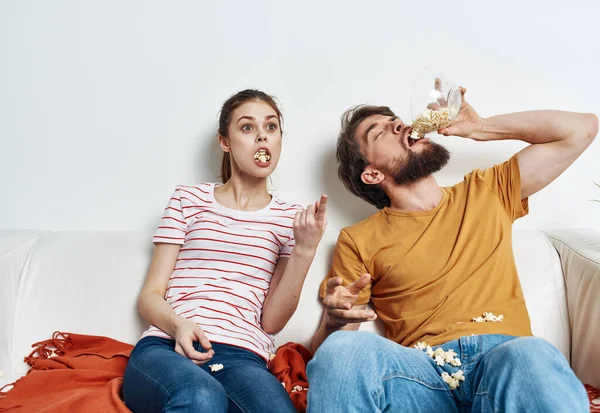 Patlamış mısır yiyen bir adam ve güzel bir kadın parlak bir odada aile dostlarıyla iletişim kuruyor.