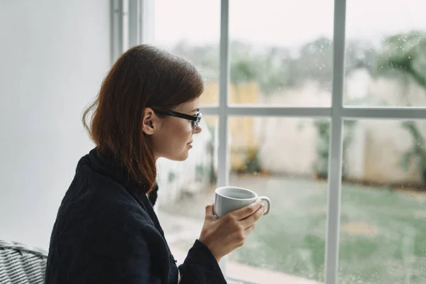 Kobieta z filiżanką kawy przy oknach na twarzy — Zdjęcie stockowe