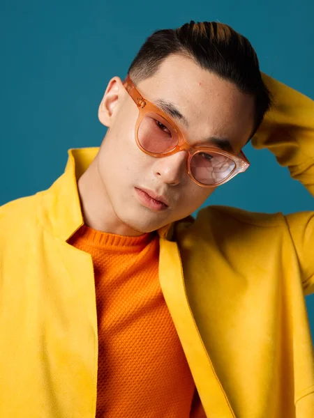 Ázsiai férfi narancssárga szemüvegben, kék háttérrel és sárga kabátban — Stock Fotó