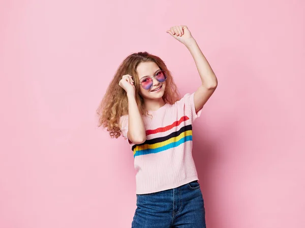 안경을 쓴 행복 한 소녀는 핑크 색 배경과 유행하는 티셔츠를 입고 춤추고 있다 — 스톡 사진