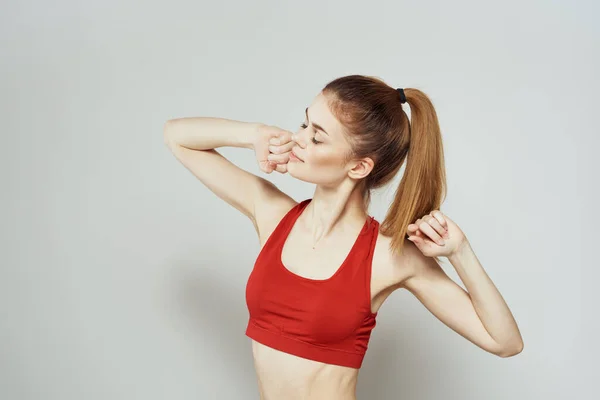 Una donna in una t-shirt rossa su uno sfondo chiaro è impegnata in gesti di fitness con le mani una figura sottile — Foto Stock