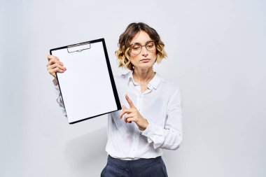 Elinde beyaz dökümanların olduğu bir klasör olan iş kadını arka planda ve saç stili gözlüklü model