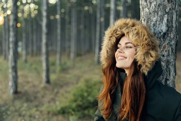 Femme souriante dans une veste dans la forêt près de l'arbre de voyage — Photo