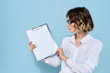 Mavi arka planda bir klasörde evrakları olan ve yüzünde açık renk gözlüklü bir iş kadını.