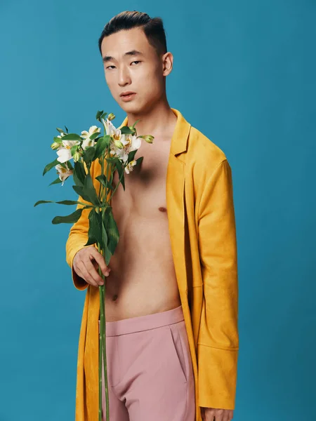 Nice guy with a bouquet of flowers on a blue background and a nude torso coat — Fotografia de Stock