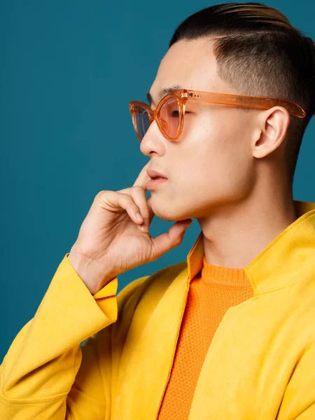 Вид сбоку на молодого человека в солнцезащитных очках и желтой куртке на синем фоне — стоковое фото