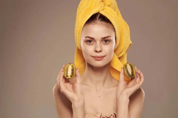 Femme avec les épaules nues avec une serviette sur sa tête kiwi dans ses mains cosmétiques de fruits de peau propre — Photo
