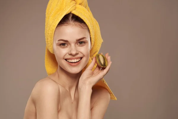 Жінка з голими плечима з рушником на голові ківі в руках чиста шкіра фруктова косметика — стокове фото