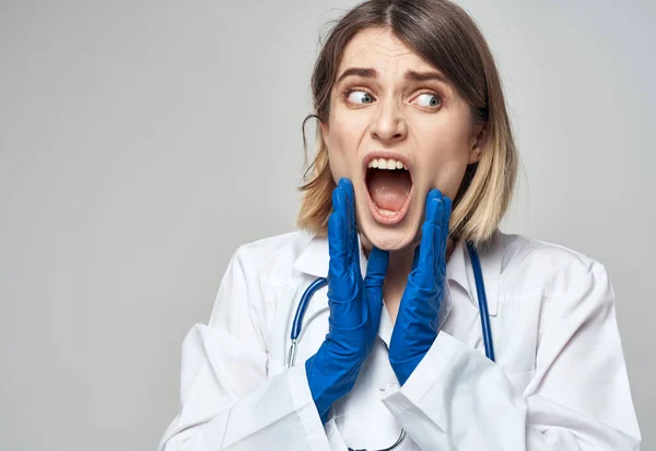 Mujer médico con la boca abierta en un vestido médico guantes azules estetoscopio —  Fotos de Stock