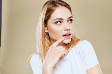 Beyaz tişörtlü neşeli bir kadın elleri bej arkaplanlı jestler yapıyor.