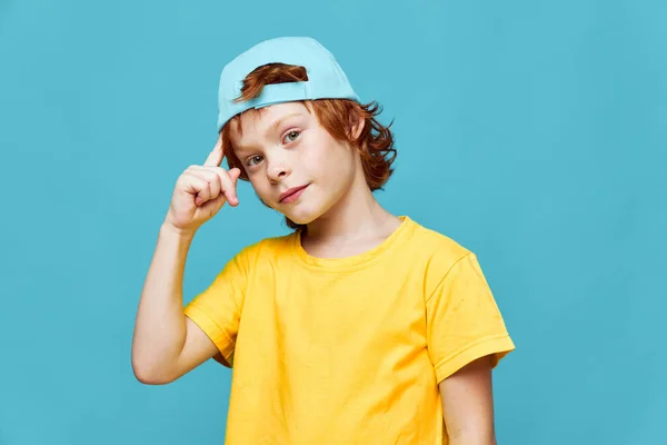 파란 모자를 쓴 빨간 머리 소년이 노란 티셔츠 스튜디오에 손을 잡고 있습니다. — 스톡 사진