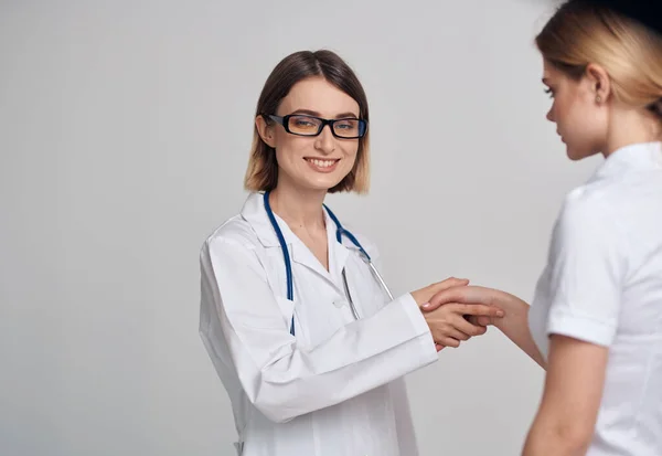 Professional doctor woman and patient shake hands on a light background