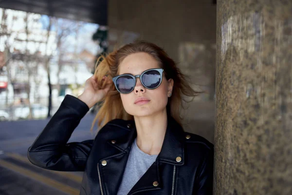 A woman stands under a bridge in the street wearing sunglasses and a leather jacket — Stock Photo, Image