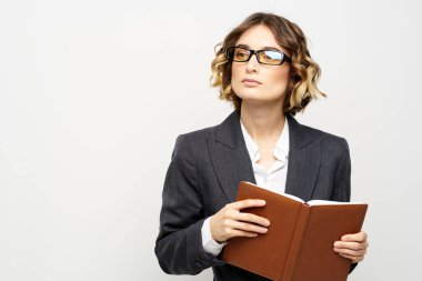 Klasik takım elbiseli bir iş kadını elinde bir not defteri ve yüzünde gözlüklerle.