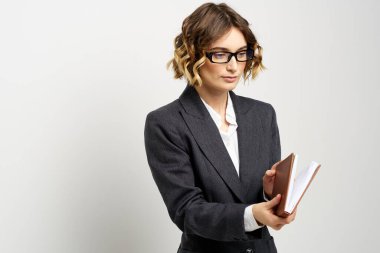 Klasik takım elbiseli bir iş kadını elinde bir not defteri ve yüzünde gözlüklerle.