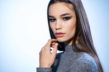 Gri kazaklı, parlak makyajlı, uzun saçlı güzel bir kadın.