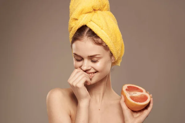 Mulher alegre com uma toalha amarela na cabeça ombros nus toranja na mão cosméticos naturais — Fotografia de Stock