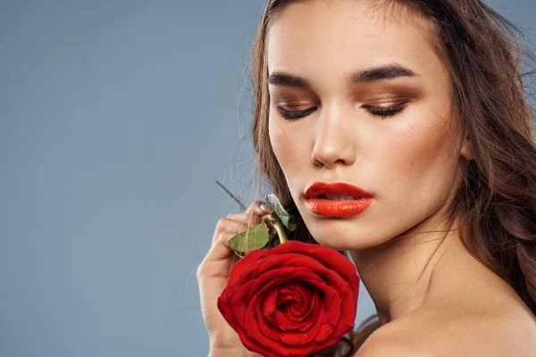 Porträt einer Frau mit einer roten Rose in den Händen auf grauem Hintergrund, nackte Schultern beim abendlichen Make-up — Stockfoto