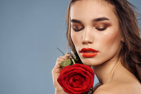 Portrait of a woman with a red rose in her hands on a gray background naked shoulders evening makeup