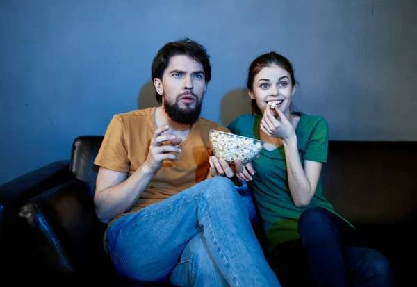 Ein emotionaler Mann und eine hübsche Frau auf der Couch schauen interessiert in einem dunklen Raum fern — Stockfoto