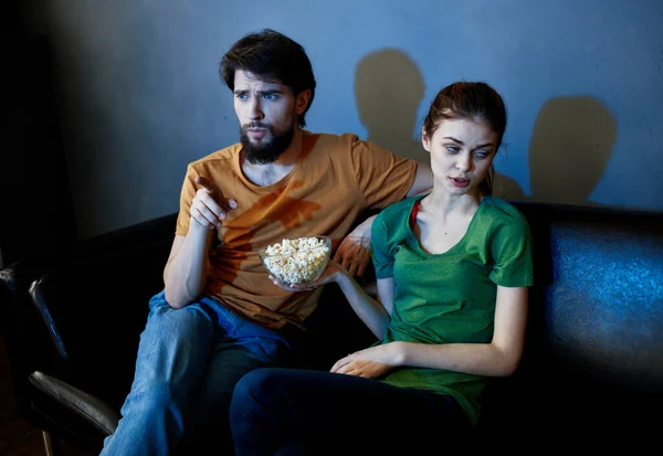 Una mujer y un hombre con palomitas de maíz en un sofá de cuero en el interior viendo la televisión por la noche — Foto de Stock