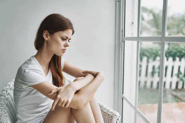 Smutna kobieta przy oknie przytula nogi i siada — Zdjęcie stockowe