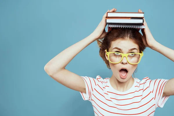 Женщина-студентка с книгами на голове и в желтых очках на синем фоне обрезанный вид — стоковое фото