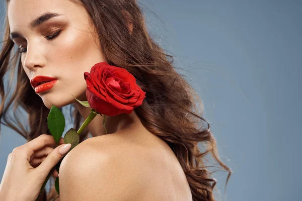 Portrait d'une femme avec une rose rouge dans les mains sur un fond gris épaules nues maquillage du soir — Photo