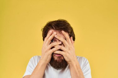 Beyaz tişörtlü bir adam, el hareketleriyle sarı arka plan manzarasını daha eğlenceli kılıyor.