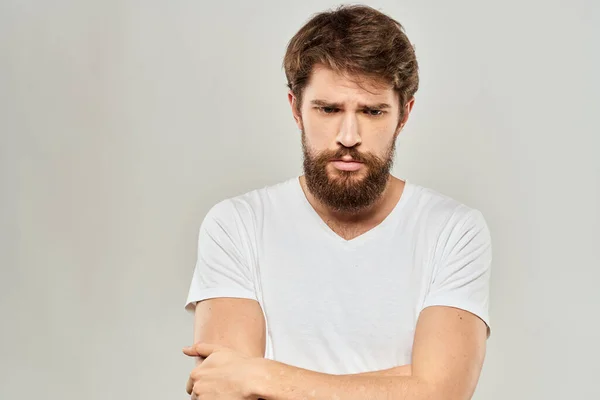 Un uomo in una t-shirt bianca con una barba emozioni scontento espressione facciale sfondo chiaro — Foto Stock