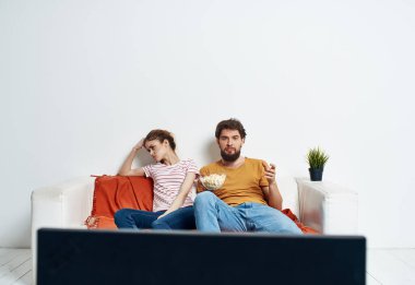 Kanepede patlamış mısırla televizyon izleyen genç adam ve kadın ve ekose yeşil çiçek.