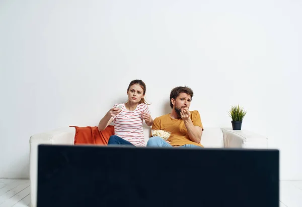 Ένας άντρας και μια γυναίκα κάθονται στον καναπέ μπροστά στην τηλεόραση και ένα πράσινο λουλούδι σε μια κατσαρόλα σε εσωτερικούς χώρους — Φωτογραφία Αρχείου
