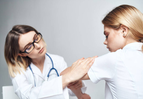 Doctor sits on a chair and woman patient indoors on a light background cropped view