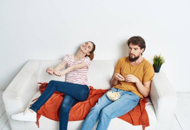 Bir kadın kanepede dinleniyor ve bir adam elinde patlamış mısır çiçeğiyle kırmızı ekose bir tencerede