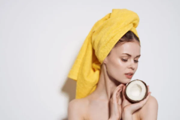 Wanita dengan bahu telanjang dengan kelapa di tangannya handuk kuning di kepalanya perawatan kulit bersih — Stok Foto