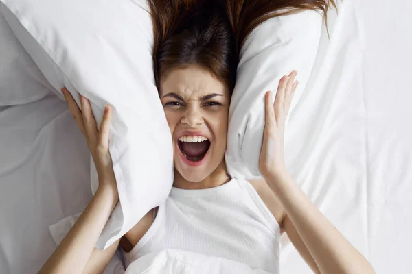 aggressive woman in bed covering her ears with pillows and shouting