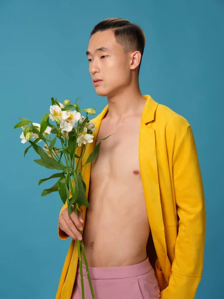 Um cara semi-nu com um buquê de flores brancas e um casaco amarelo em um fundo azul — Fotografia de Stock