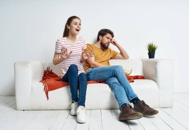 Çizgili tişörtlü bir kadın ve parlak bir odada televizyon izleyen bir adam.