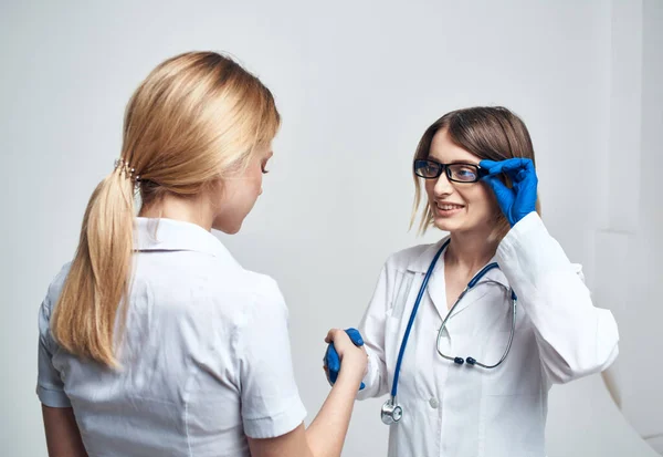 护士以浅色背景与病人握手，并用听诊器与蓝色手套握手 — 图库照片