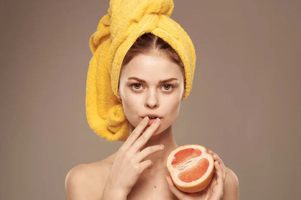 Mulher alegre com uma toalha amarela na cabeça ombros nus toranja na mão cosméticos naturais — Fotografia de Stock