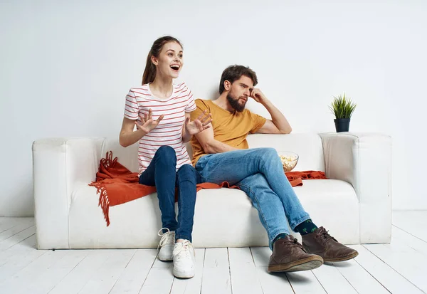 Μια γυναίκα με ριγέ μπλουζάκι και ένας άντρας στον καναπέ να βλέπει τηλεόραση σε ένα φωτεινό δωμάτιο. — Φωτογραφία Αρχείου