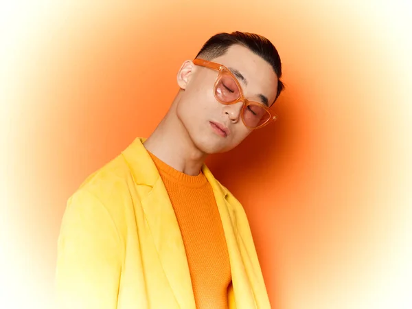 Hombre de moda en un suéter amarillo sobre un fondo naranja y gafas en su cara, aspecto asiático — Foto de Stock
